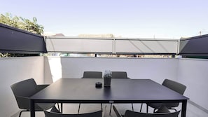 Un patio al aire libre con una mesa, sillas, una planta en maceta y vista a edificios al fondo.
