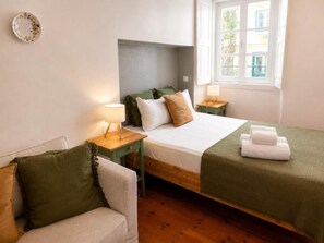 Un dormitorio con una cama, una mesita de noche con lámpara, una silla y una ventana.