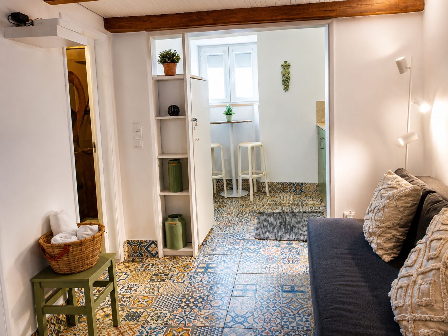 A room with a patterned floor, a sofa, a small table with a basket, and a door leading to another room.