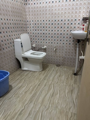 A bathroom with a toilet, a sink, and a blue bucket. - Radha Madhav Kutir (Vrindavan)