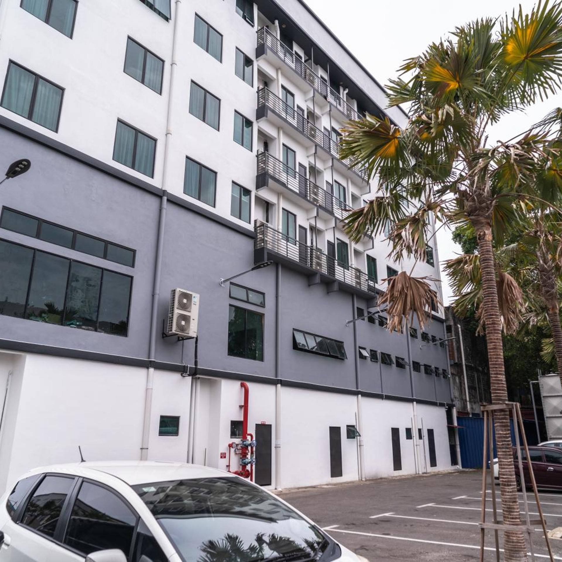 A multi-story building with a white facade, air conditioning units, and a parking lot with a white car.