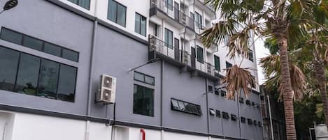 A multi-story building with a white facade, air conditioning units, and a parking lot with a white car.