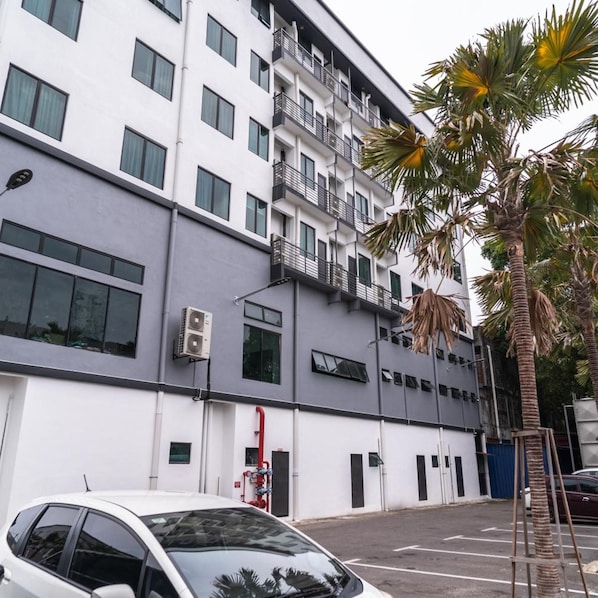 Un edificio a più piani con facciata bianca, condizionatori d'aria e un parcheggio con un'auto bianca.