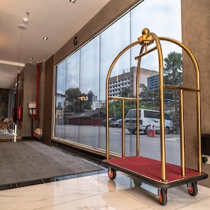 Una hall d'albergo con un'ampia finestra, un ascensore con cornice dorata e una zona tappezzata di rosso.