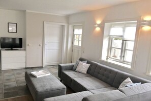 A modern living room with a grey sectional sofa, a flat-screen TV, and a dining area with a white cabinet. - 4 "Northern tip" in Letj Reethüs (Norddorf)