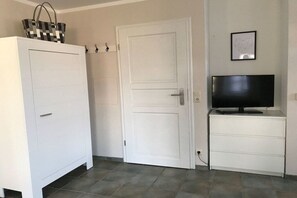 A room with a white wardrobe, a closed door, a television on a white cabinet, and a framed picture on the wall. - 4 "Northern tip" in Letj Reethüs (Norddorf)