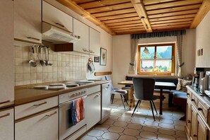 Eine Küche mit Herd, Spüle und Schränken, ein Essbereich mit Tisch und Stühlen sowie ein Fenster mit Blick ins Freie.