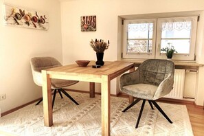 Ein Essbereich mit einem Holztisch und zwei Stühlen, einer Vase mit Trockenpflanzen und Kunstwerken an den Wänden.