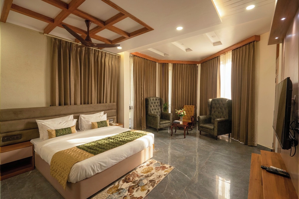 Una habitación de hotel con una cama grande, dos sillones, una mesita y un televisor.