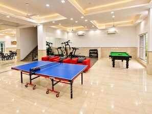 A spacious indoor area with a ping pong table, exercise equipment, and a billiards table. - Executive Suite With Balcony-1Bhk Luxury Apartment, Sector 43 Gurugram (Gurugram)