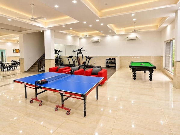 Un'ampia area interna con tavolo da ping pong, attrezzature per esercizi fisici e tavolo da biliardo.