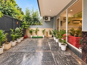 Un cortile con piante in vaso, pavimento in piastrelle grigie e un edificio moderno con ampie finestre e un condizionatore.