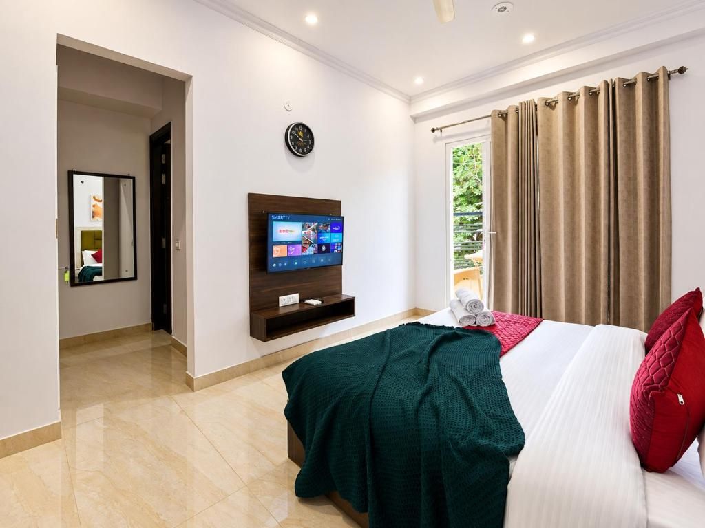 Een hotelkamer met een bed, een televisie, een klok en een raam met gordijnen.