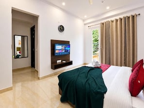 Una camera d'albergo con un letto, una televisione, una sveglia e una finestra con tende.