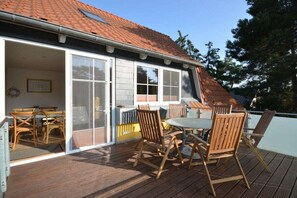 Une terrasse avec une table et des chaises, une porte-fenêtre coulissante donnant sur une pièce et un toit recouvert de tuiles rouges.