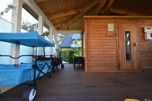 Ein überdachter Außenbereich mit einer Holzhütte, einer überdachten Sitzgelegenheit mit Kinderwagen und einem kleinen Tisch.