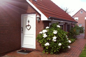 A brick house with a white door, a heart-shaped decoration, and white hydrangea bushes. - KrosseKrabbeNorddeich (Norden-Norddeich)