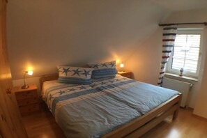 A bedroom with a bed, bedside lamps, a window with curtains, and a radiator. - KrosseKrabbeNorddeich (Norden-Norddeich)