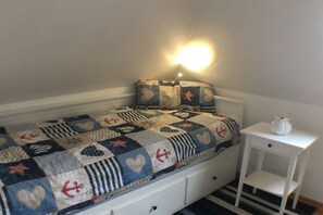 A single bed with a quilt, a bedside table with a lamp, and a small drawer unit. - KrosseKrabbeNorddeich (Norden-Norddeich)