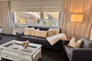A modern living room with a dark grey sofa, a glass coffee table, and a lamp. - Baltic Home near the beach (Kühlungsborn, Ostseebad)