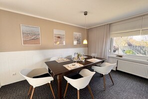 A dining area with a table set for four, white chairs, and framed artwork on the wall. - Baltic Home near the beach (Kühlungsborn, Ostseebad)