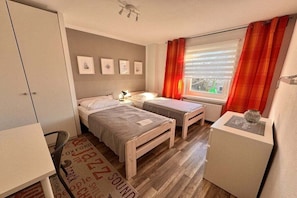 A compact room with two single beds, a desk, a radiator, and a window with curtains. - Baltic Home near the beach (Kühlungsborn, Ostseebad)