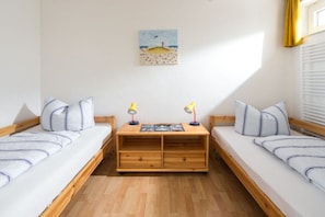 A room with two single beds, a wooden desk with two lamps, and a beach-themed painting on the wall. - House North Sea View 142 (Norderney)