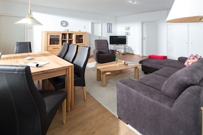 A modern living room with a dining table, chairs, a sofa, a TV, and a cabinet. - House North Sea View 142 (Norderney)