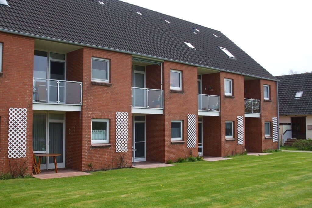 A multi-story residential building with balconies, a flat roof, and a well-maintained lawn.