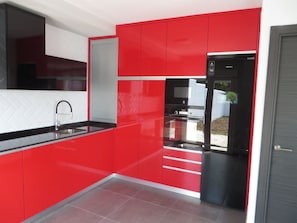 A modern kitchen with red cabinetry, a black refrigerator, and a stainless steel sink.