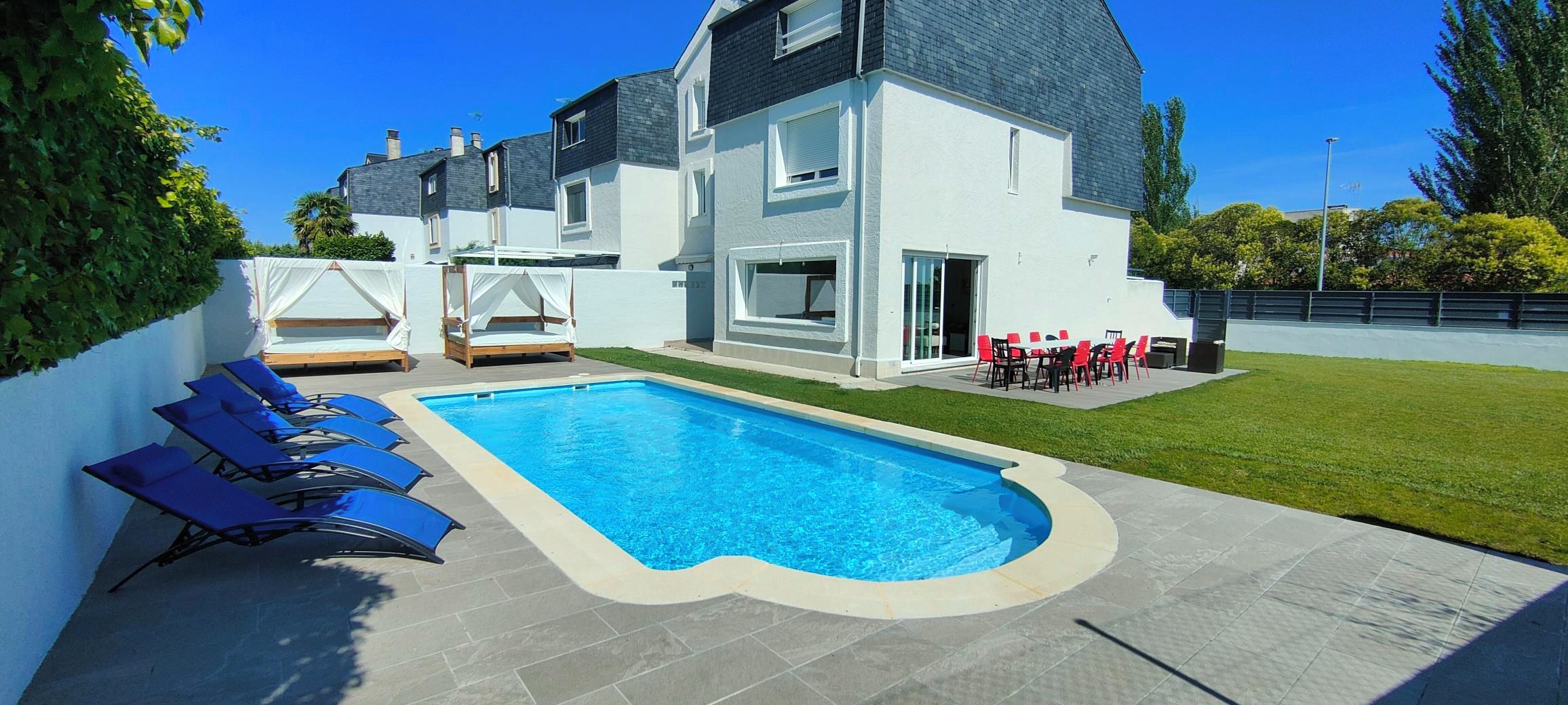 Una casa moderna de dos pisos amb piscina, mobiliari d'exterior i un jardí ben cuidat.