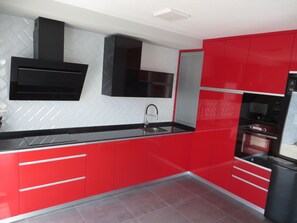 A modern kitchen with red cabinetry, a black countertop, and a built-in oven.