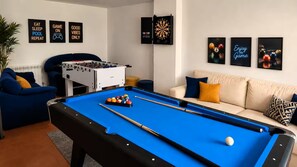 A pool table with a foosball table and billiard balls, a sofa with cushions, and wall art.