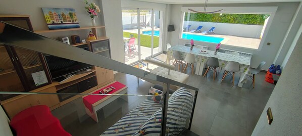 A modern living room with a TV, seating, and a view of a pool.