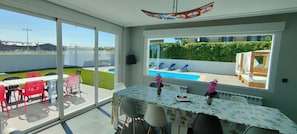 A dining area with a view of a swimming pool and a garden.