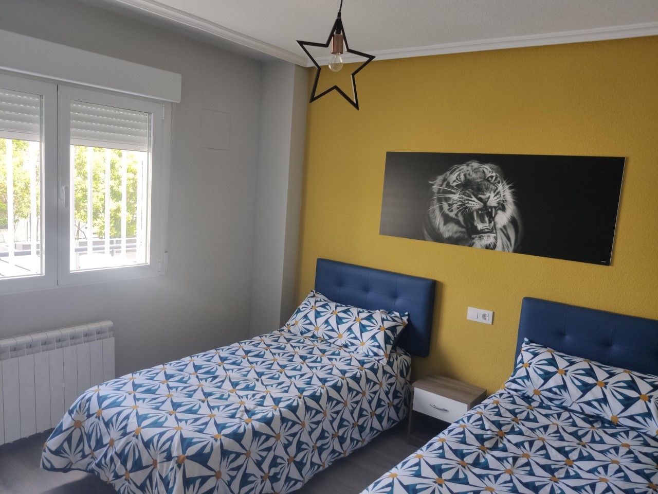 Un dormitorio con dos camas, una lámpara en forma de estrella y un estampado animal grande en la pared.