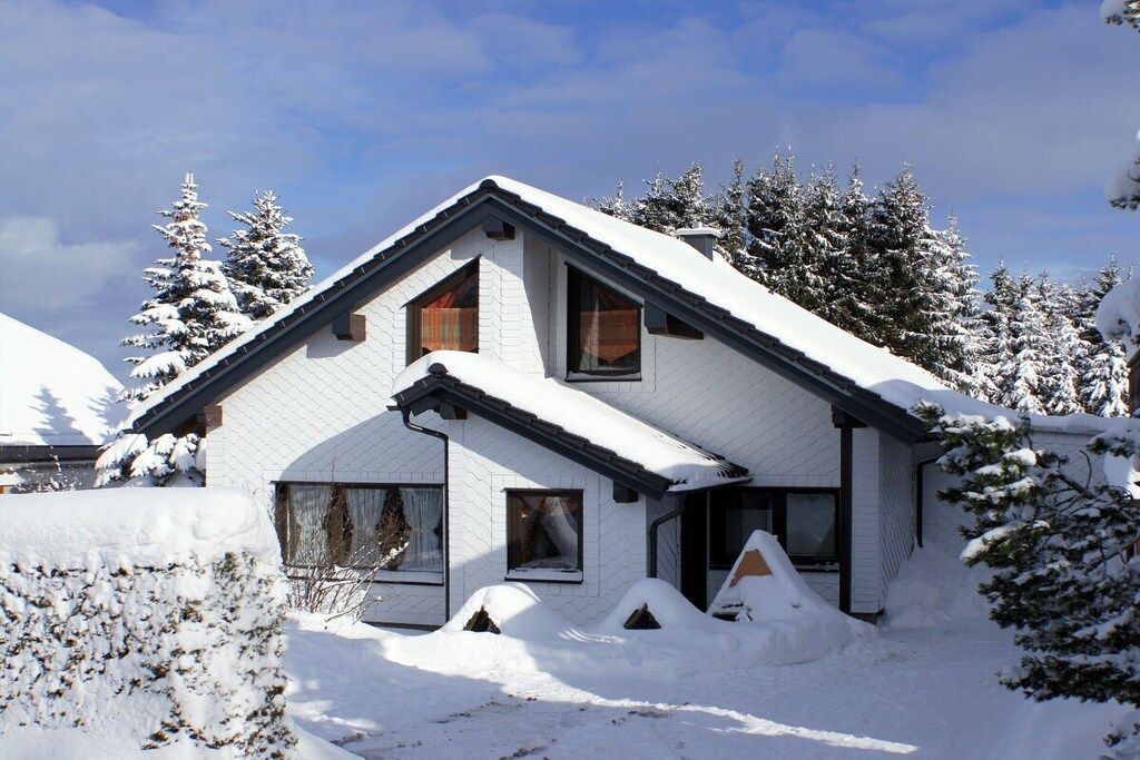 Ein zweistöckiges Haus mit geneigtem, mit Schnee bedecktem Dach, umgeben von schneebedeckten Bäumen.