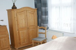 A bedroom with a wooden wardrobe, a chair, a bed, and a window with curtains. - Holiday apartment with 2 bedrooms (Heringsdorf)