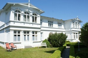 A large, white, two-story building with a symmetrical facade, large windows, and a well-maintained garden with a paved path. - Holiday apartment with 2 bedrooms (Heringsdorf)