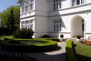 A white building with a paved courtyard, a bench, and a well-maintained hedge. - Holiday apartment with 2 bedrooms (Heringsdorf)