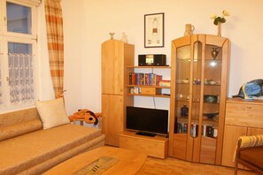 A living room with a sofa, a television, a wooden cabinet with glass doors, and a window with curtains. - Holiday apartment with 2 bedrooms (Heringsdorf)