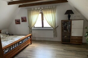 A bedroom with a wooden bed, a radiator, a cabinet, and a window with curtains. - Holiday home with 2 bedrooms (Wurster Nordseeküste)