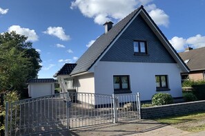 A two-story house with a sloped roof, a gated driveway, and a clear blue sky. - Holiday home with 2 bedrooms (Wurster Nordseeküste)