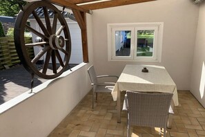 Une terrasse avec une table et des chaises, une grande roue en bois et une fenêtre.