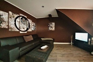 Ein modernes Wohnzimmer mit einem schwarzen Ledersofa, einem Couchtisch und einem Flachbildfernseher auf einem Standfuß.