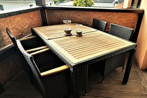 A wooden table with four chairs on a balcony, two glasses on the table, and a view of buildings in the background. - Holiday apartment with 3 bedrooms (Karlshagen)