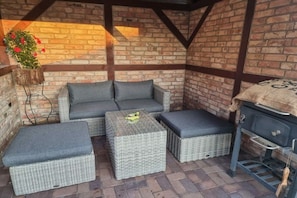 A covered outdoor seating area with wicker furniture and a barbecue grill. - Holiday apartment with 3 bedrooms (Karlshagen)