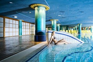 An indoor swimming pool with a tiled floor and a person sitting on the edge. - Holiday apartment with 3 bedrooms (Karlshagen)
