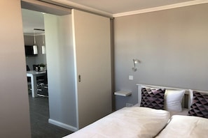A bedroom with two beds, a bedside table, and a small shelf with decorative pillows. - Holiday apartment with 2 bedrooms (Westerland)