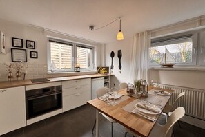 A modern kitchen with a dining area, featuring a wooden table set for two, a built-in oven, and a window with a view. - Kühlungsborn - SeaSide No. 6 (Kuehlungsborn)